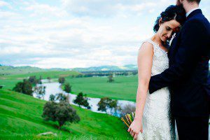 bride and groom embracing on hilltop at forges hut Kimo Estate. lagoon in background with green pastures of the farm