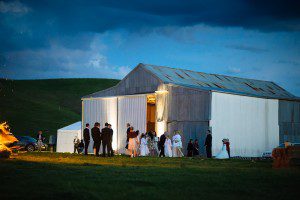 guests around a shed in the country at a wedding, bonfire burning in the foreground