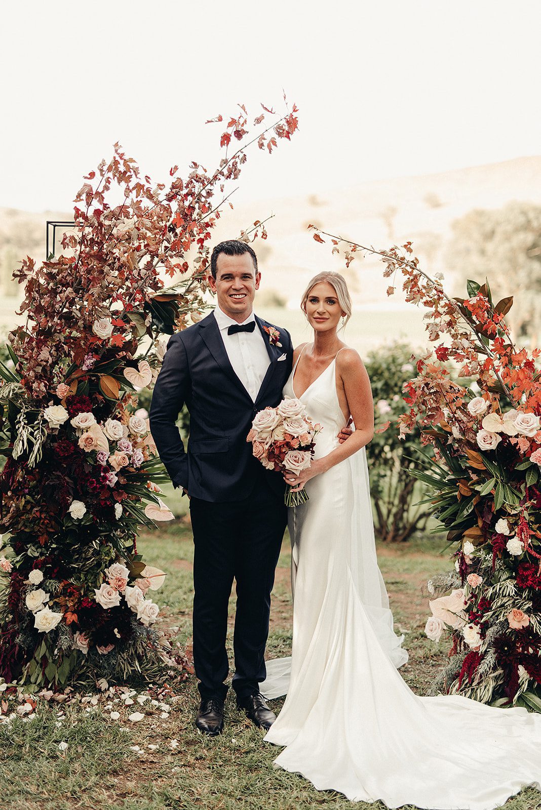 A beautiful bride and groom stand by the wedding arbour on a farm in country nsw.