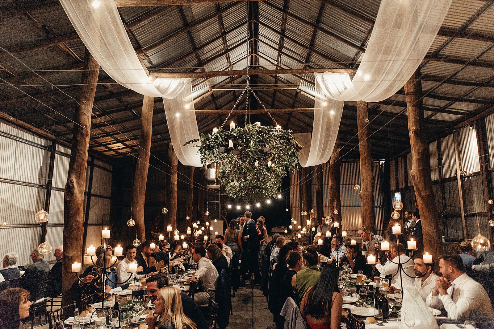 A barn wedding venue with cathedral ceilings. It's lit by candle light. guests eat their dinner at the wedding reception venue.