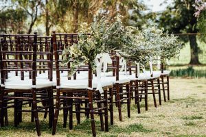 wedding chairs set up with floral arrangements on the side of aisle.