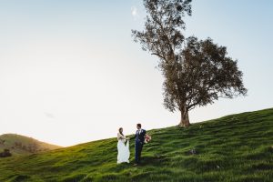 loving wedding couple frolicking in the green grass under a gum tree at Biome Estate. happy memories being made