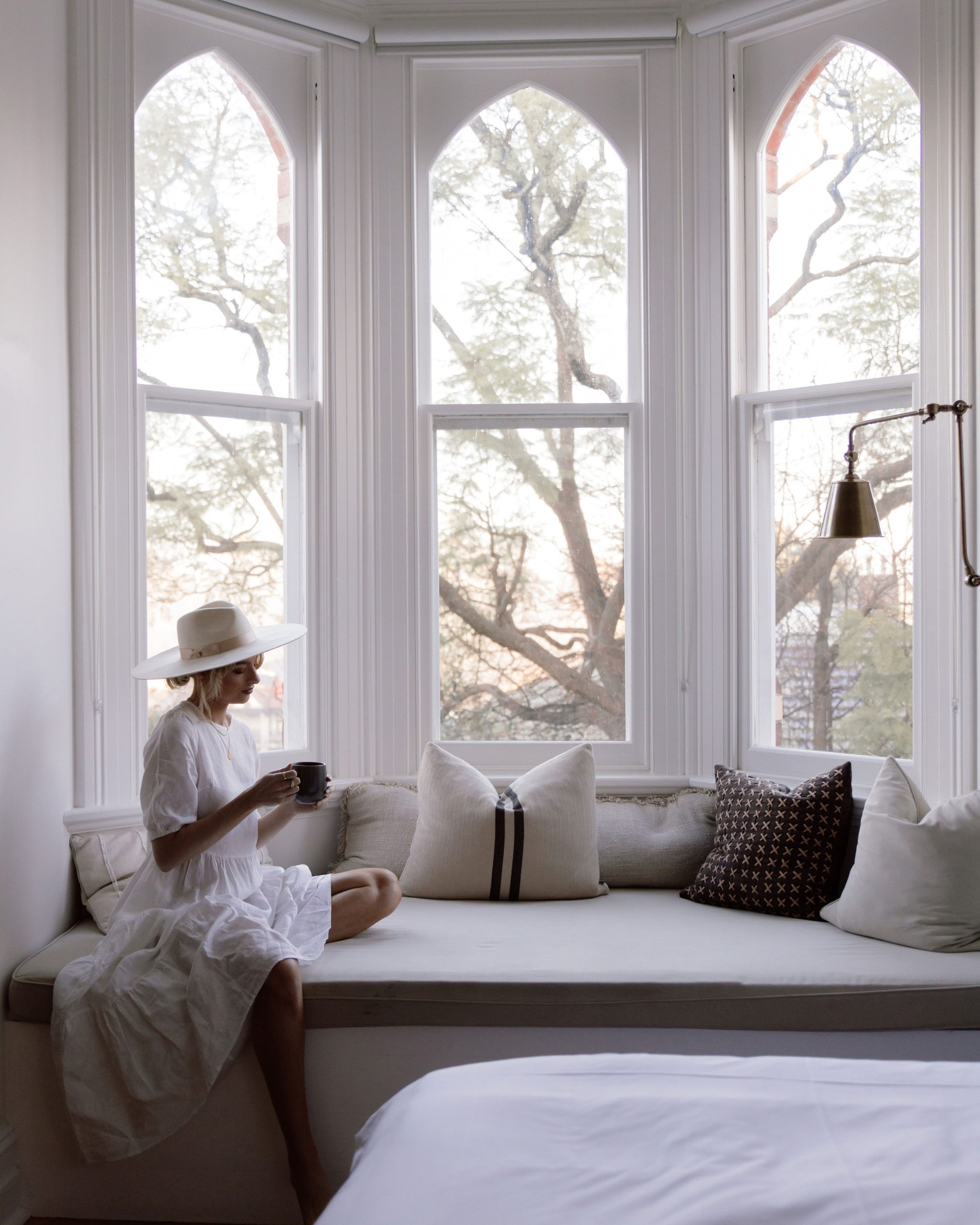 woman sitting in the bay windows with a cup of tea in linen skirt on bay window seat with comfy cushions