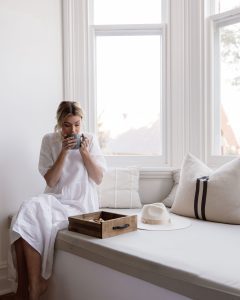 woman enjoying her tea, neutral tones and varying textures with comfy cushions on window seat