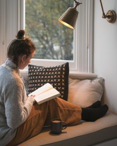 girl reading book with a cup of tea in a window seat covered in comfy pillows