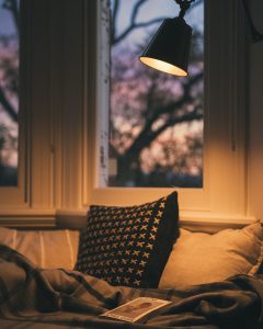 window seat bathed in light from wall lamp, wooden blanket and comfy pillows