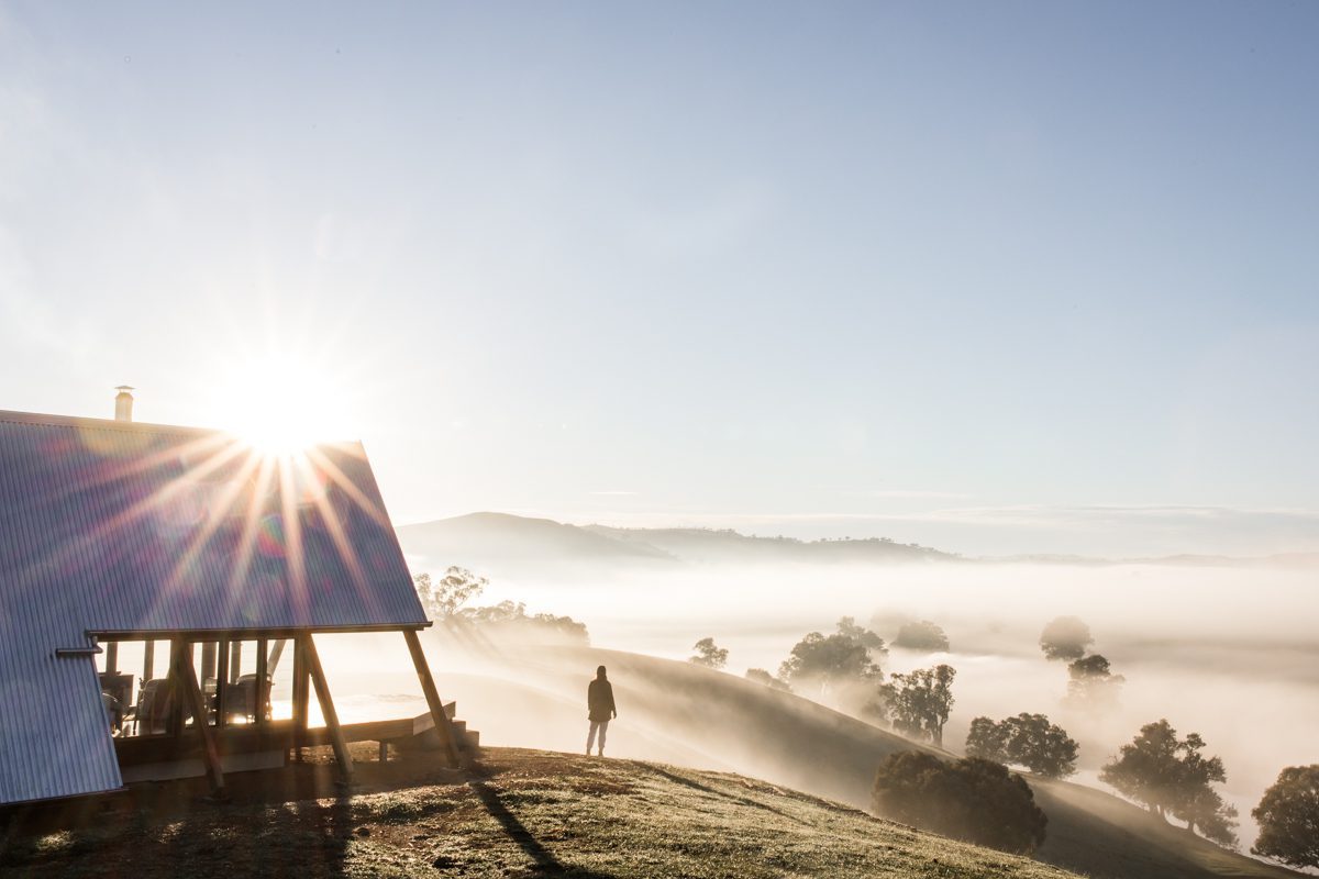 eco hut on hill with fog and a traveller looking over the flats