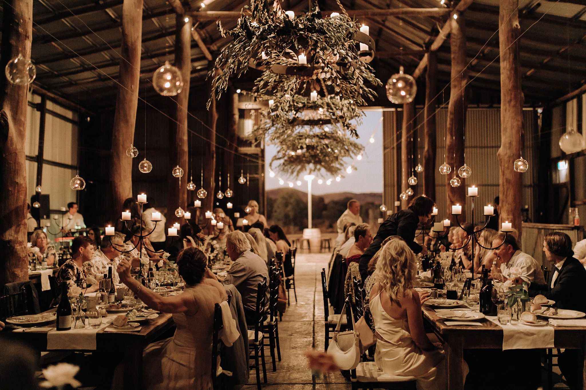 A beautiful wedding reception with flowers and guests enjoying a meal. Flowers hanging from the roof and candles lighting the reception