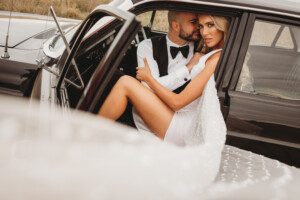 A Bride and groom in a clasic car. The groom is besotted by his new wife
