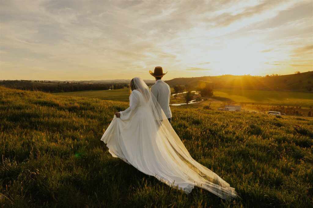couple walking across a hill on their wedding day. A beautiful country scene in the background