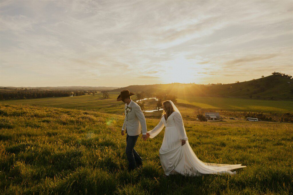a beautiful golden scene at sunset of a bride and groom, hand in hand on their wedding day