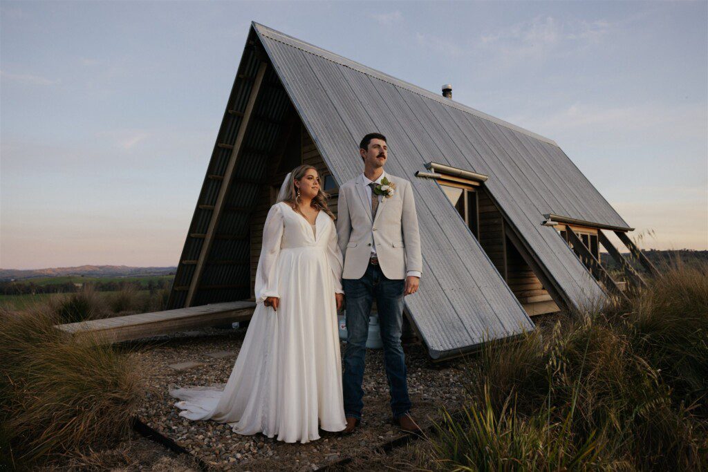 Bride and groom standing proudly in front of an a-frame cabin