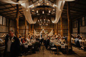 A huge barn Wedding Reception Venue with linen draping from the beams. The room is candlelit and theres two long tables of wedding guests