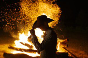 Groom tipping his hat at night standing in front of the roaring bonfire