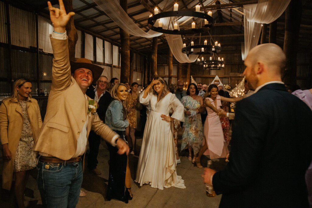 The bride looks embarrassed and is laughing at the behaviour of her dear friends at the wedding reception, guests are dancing